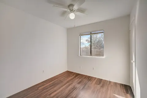 an empty room with wooden floor ceiling fan and windows