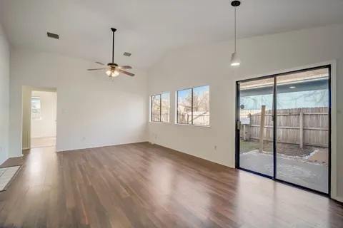 a view of an empty room with wooden floor and fan
