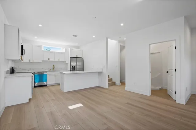 a large kitchen with kitchen island a sink a stove a refrigerator and white cabinets with wooden floor