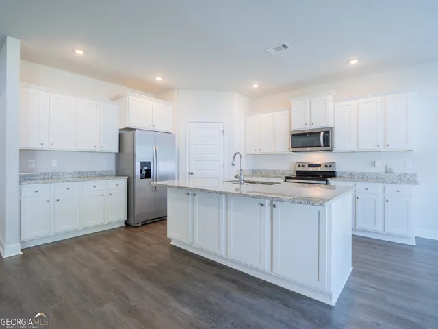 a view of empty room with wooden floor and kitchen