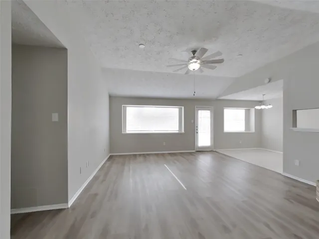 an empty room with wooden floor chandelier fan and windows