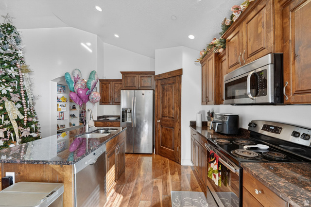 141 Wolverine Creek Elk Ridge, UT 84651 - Photo 10 of 47 Kitchen with stainless steel appliances, dark stone countertops, light wood-style floors, vaulted ceiling, and a center island with sink