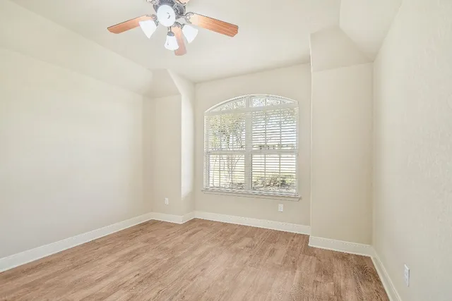 an empty room with wooden floor chandelier fan and windows