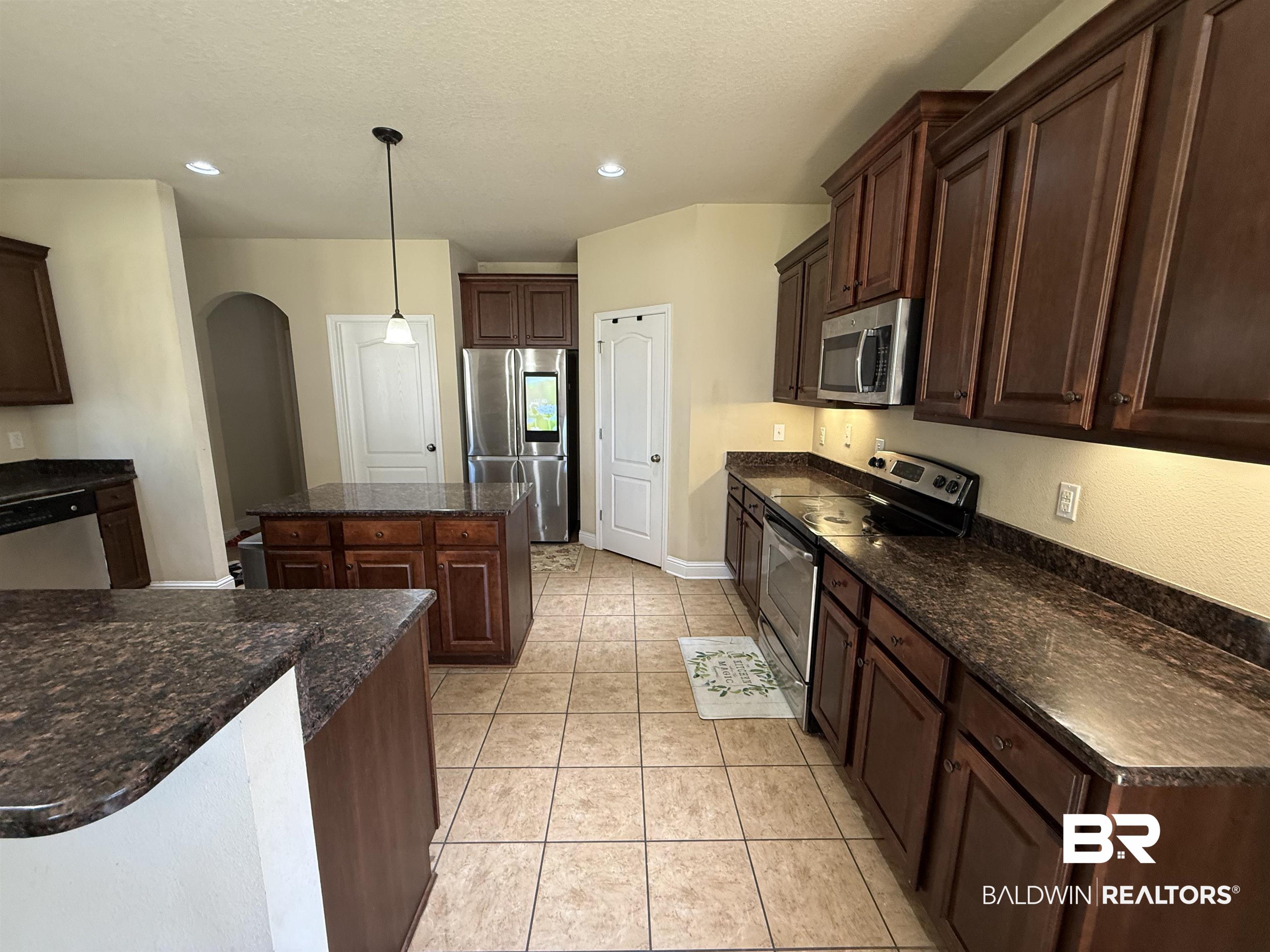 9023 Krystal Ridge Court Daphne, AL 36526 - Photo 15 of 41 Kitchen featuring dark brown cabinetry, appliances with stainless steel finishes, a center island, decorative light fixtures, and light tile patterned floors