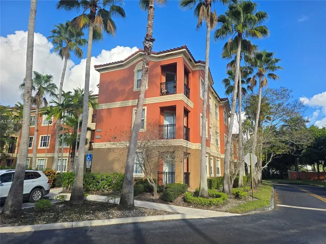 a front view of a multi story residential apartment building with yard and parking