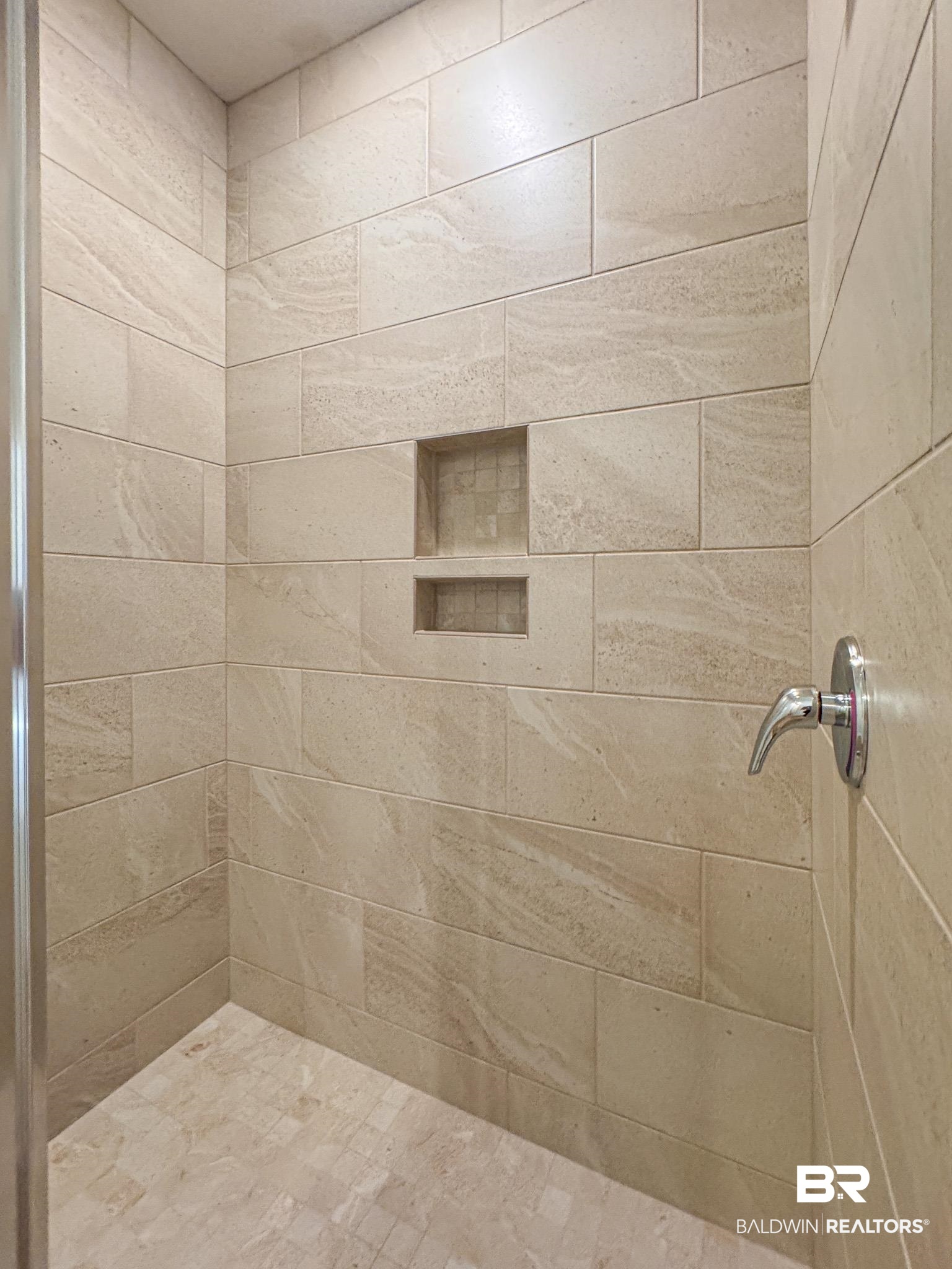 18151 Kent Circle Foley, AL 36535 - Photo 9 of 25 Spacious shower stall featuring light-toned rectangular wall tiling, dual recessed niches, a coordinating mosaic tile floor, and a polished chrome shower fixture
