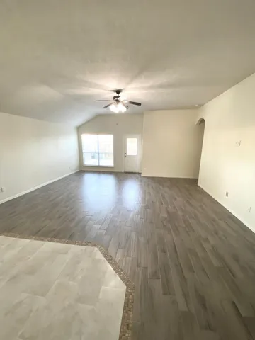 an empty room with wooden floor chandelier fan and windows