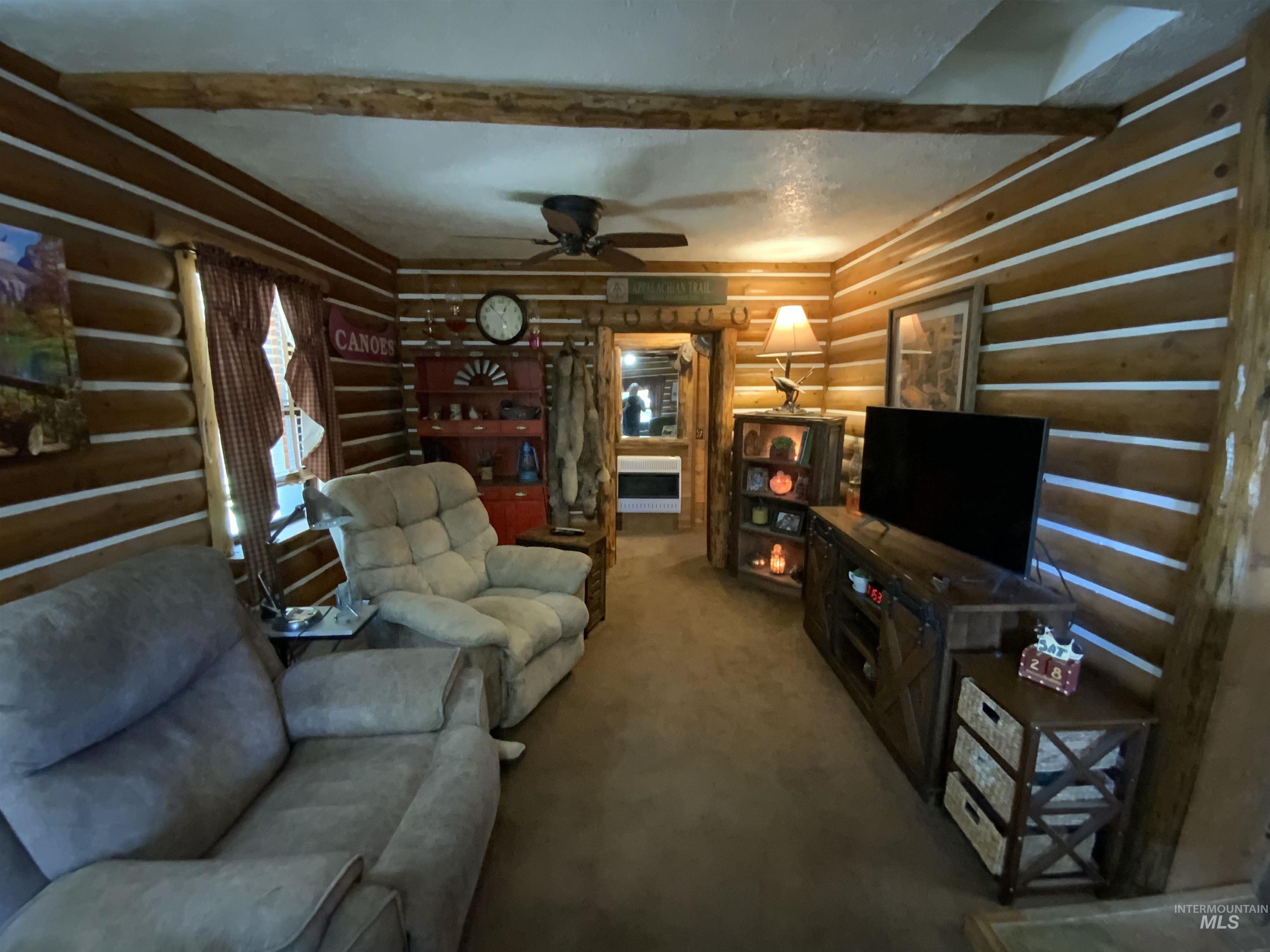 205 Alturas Avenue East Fairfield, ID 83327 - Photo 38 of 39 Carpeted living room featuring rustic walls, beamed ceiling, and a ceiling fan