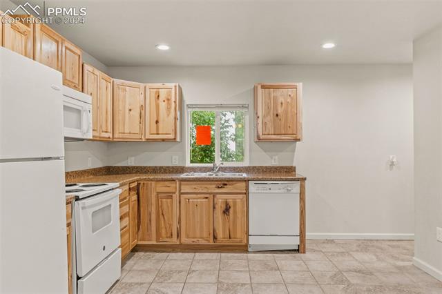 Kitchen with light brown cabinets, dark stone counters, sink, light tile floors, and white appliances
