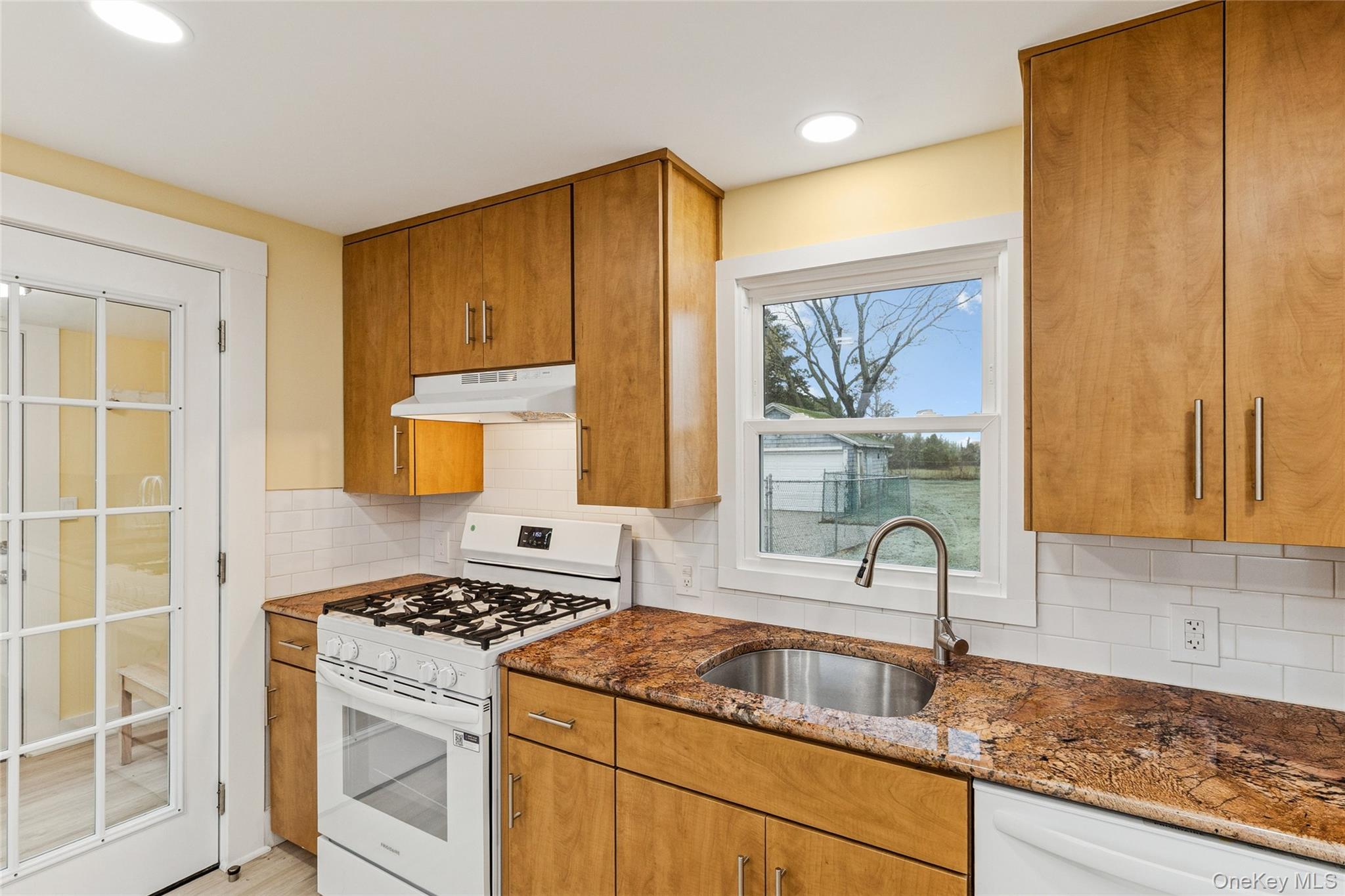 17425 County Road 48 Cutchogue, NY 11935 - Photo 21 of 30 Kitchen with white appliances, brown cabinets, dark stone countertops, under cabinet range hood, and backsplash