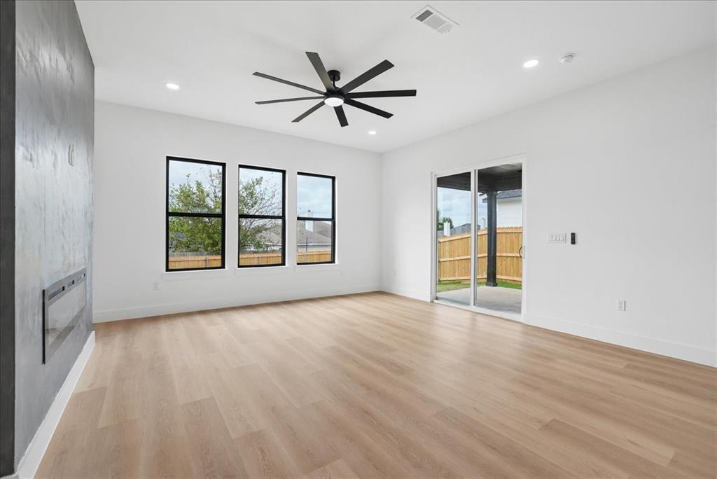 1648 West Wintergreen Road Lancaster, TX 75134 - Photo 13 of 23 Spacious room featuring light wood-finish flooring, a contemporary ceiling fan, recessed lighting, a built-in linear fireplace, and an expansive sliding glass door to the exterior