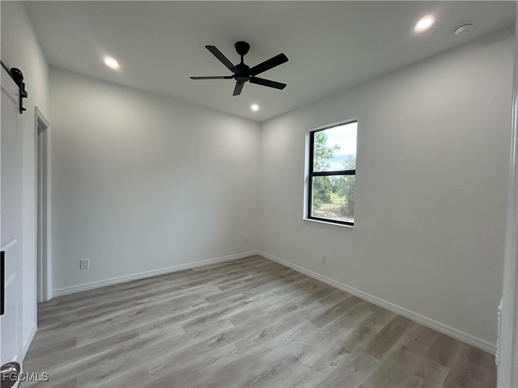 449 Bell Boulevard Lehigh Acres, FL 33974 - Photo 6 of 21 an empty room with wooden floor ceiling fan and windows