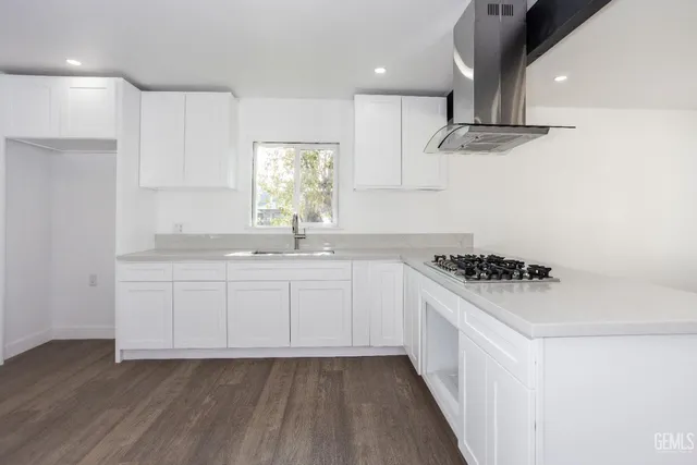 a kitchen with granite countertop a sink dishwasher a stove and white cabinets with wooden floor