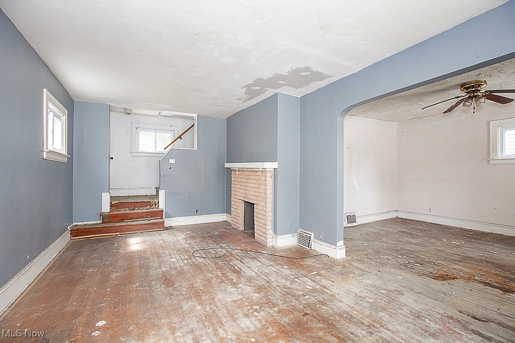 3538 Independence Road Cleveland, OH 44105 - Photo 3 of 24 Unfurnished living room with hardwood / wood-style flooring, ceiling fan, arched walkways, stairway, and a brick fireplace