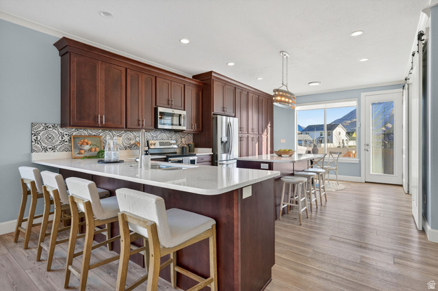 1222 West 190th Street North Mapleton, UT 84664 - Photo 10 of 46 Expansive kitchen featuring a large island with seating, rich wood cabinetry, a decorative tile backsplash, stainless steel appliances, and wood-finish flooring