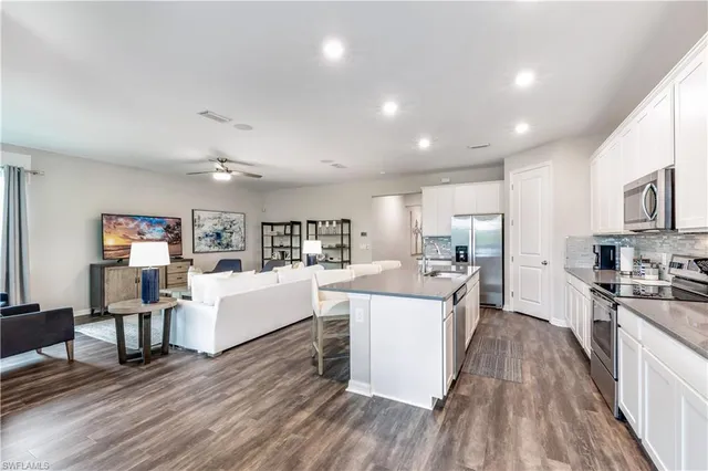 a living room with stainless steel appliances granite countertop furniture wooden floor a rug and a kitchen view