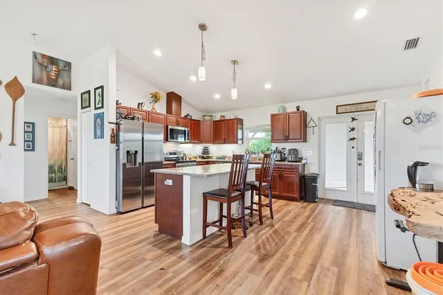 a kitchen with stainless steel appliances kitchen island granite countertop a refrigerator a stove top oven and a dining table with wooden floor