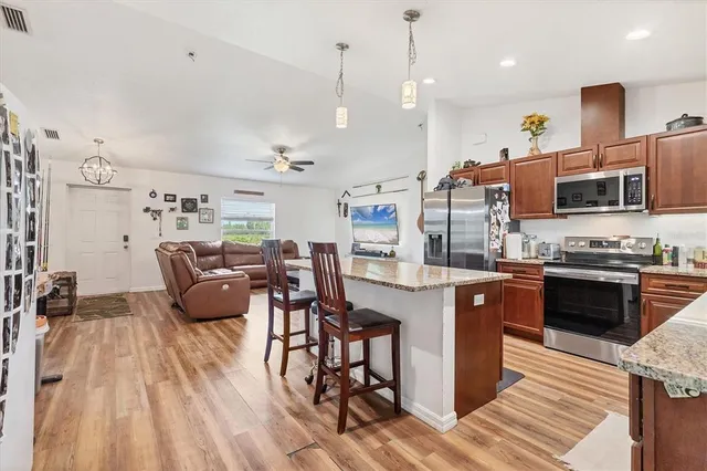 a open kitchen with stainless steel appliances granite countertop a stove top oven a sink dishwasher a dining table and chairs with wooden floor