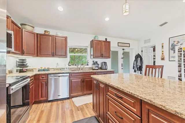 a kitchen with stainless steel appliances granite countertop a stove top oven a sink dishwasher and cabinets with wooden floor