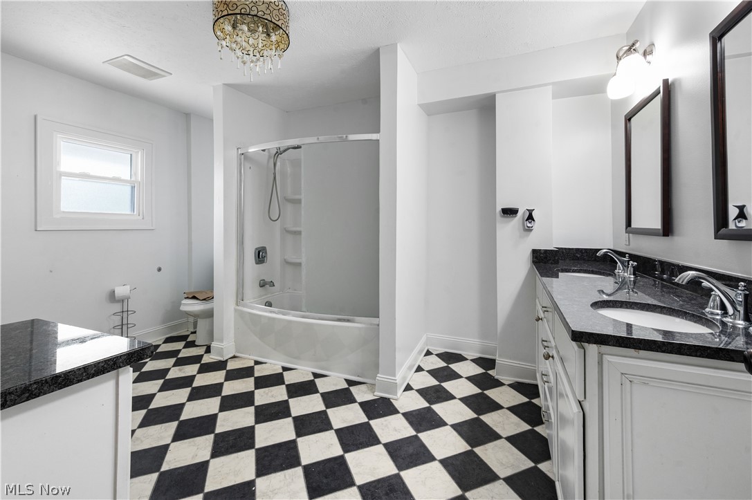 371 Merriman Road Akron, OH 44303 - Photo 16 of 27 Bathroom featuring striking black and white checkered flooring, a double vanity with dark countertops and integrated sinks, a white tub and shower combination, and a window for natural light