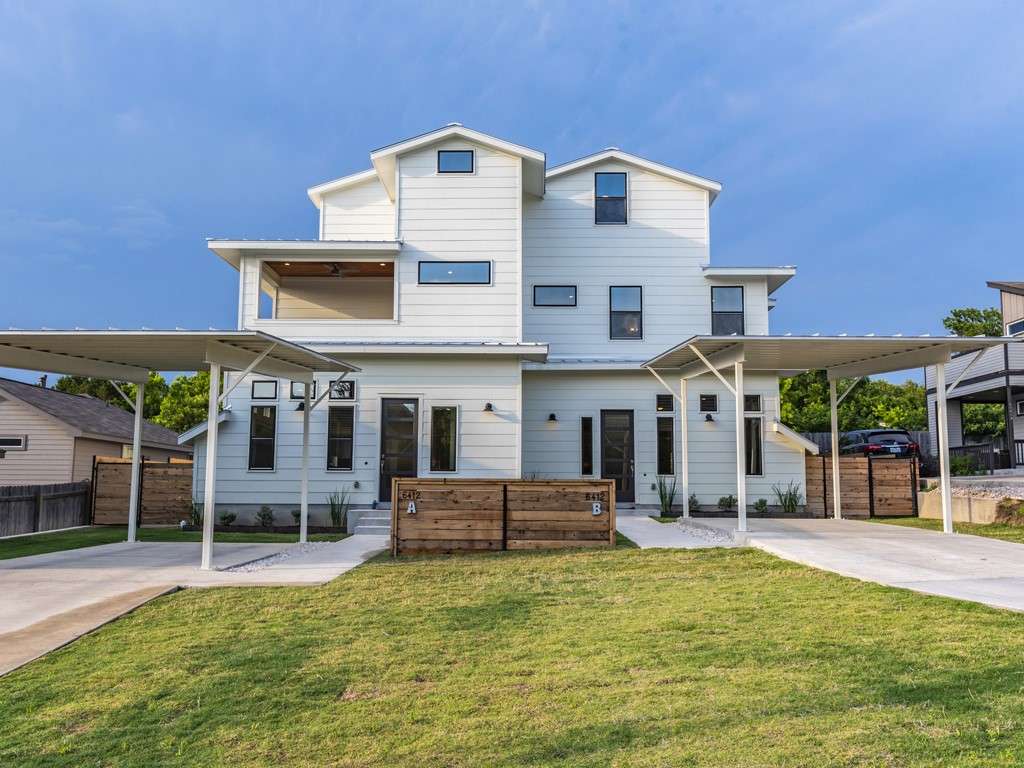 6412 Carson Ridge, Unit B Austin, TX 78741 - Photo 28 of 29 Contemporary duplex exterior featuring a light-colored facade with dark-framed windows, a covered second-story balcony, two carport structures, and a manicured lawn