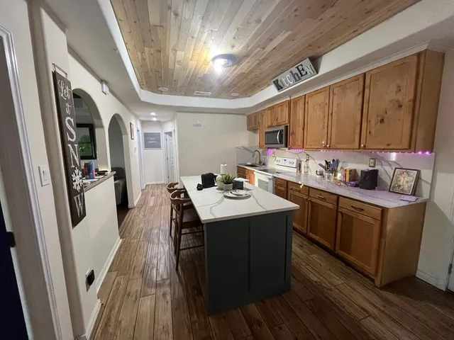 a kitchen with stainless steel appliances granite countertop a refrigerator a sink dishwasher a stove and white countertops with wooden floor