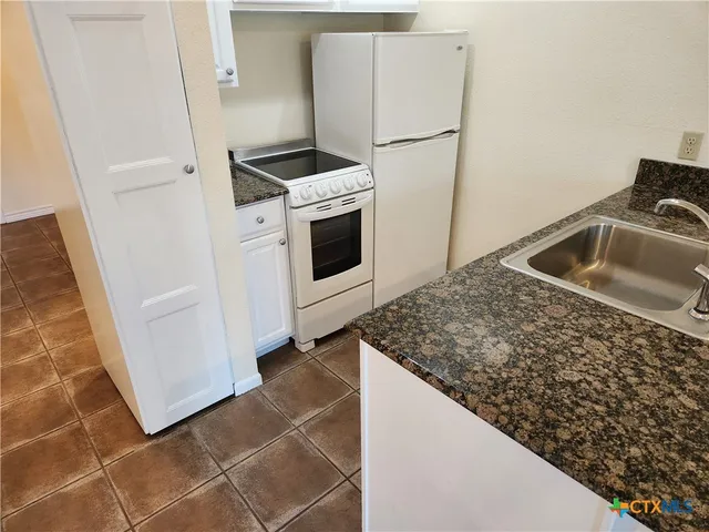 a kitchen with granite countertop a sink stove and refrigerator