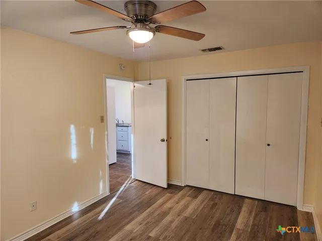 a view of an empty room with wooden floor and a ceiling fan
