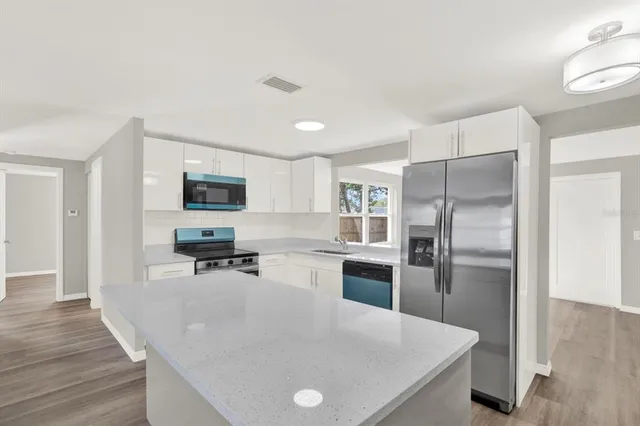 a kitchen with stainless steel appliances granite countertop a refrigerator a stove a sink a microwave and white cabinets with wooden floor