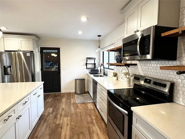 a kitchen with stainless steel appliances kitchen island granite countertop a refrigerator a stove a sink a dining table and chairs with wooden floor