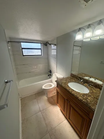 a bathroom with a granite countertop sink a toilet a mirror and bathtub