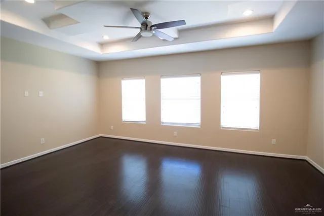 an empty room with wooden floor and windows with curtains