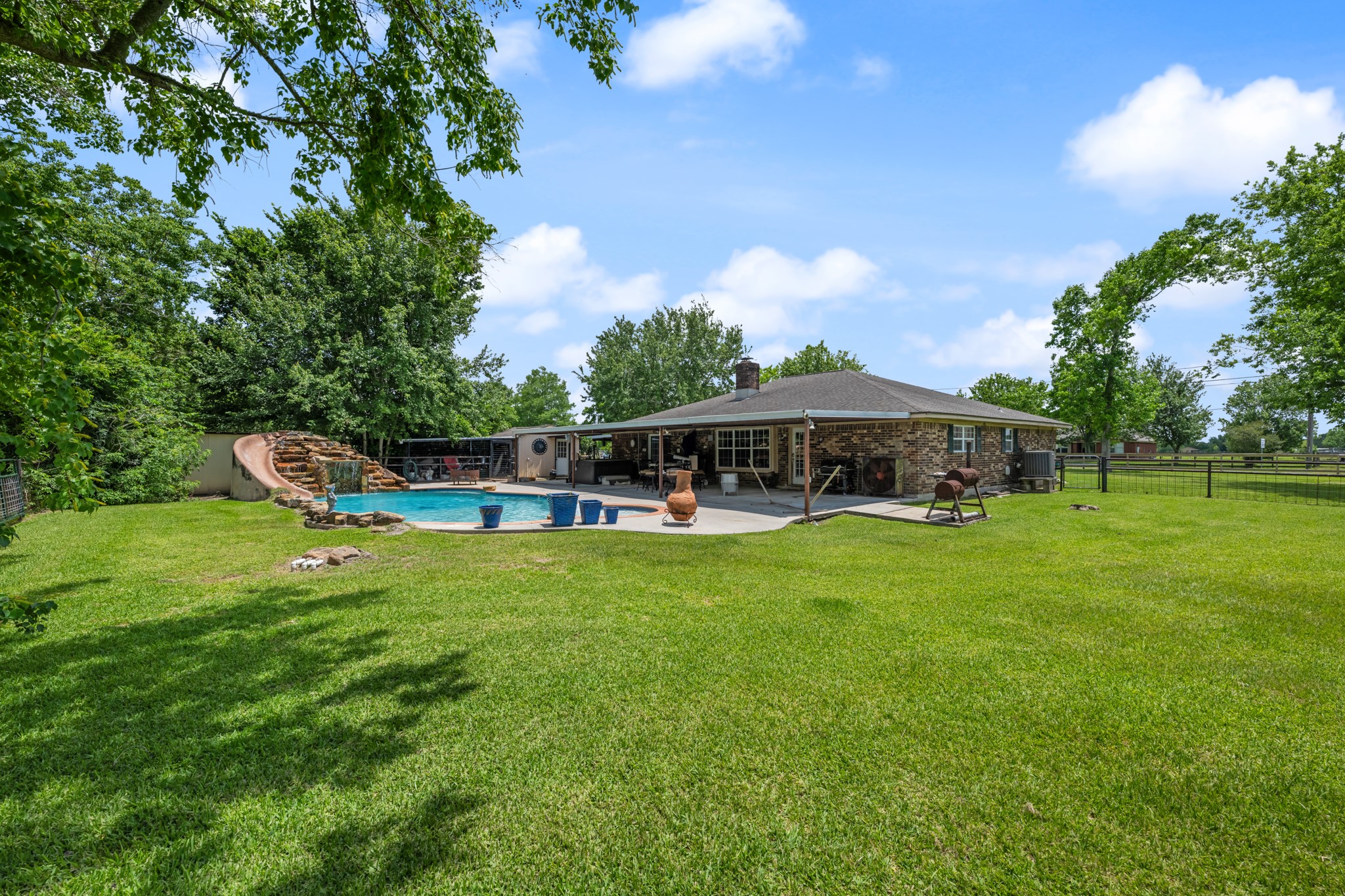 15602 Fir Road Santa Fe, TX 77517 - Photo 29 of 42 Expansive backyard retreat featuring a resort-style pool with rock waterfall slide, large covered patio, and plenty of open green space to enjoy. Mature trees and fenced surroundings create a private setting ideal for entertaining, recreation, or relaxing outdoors.