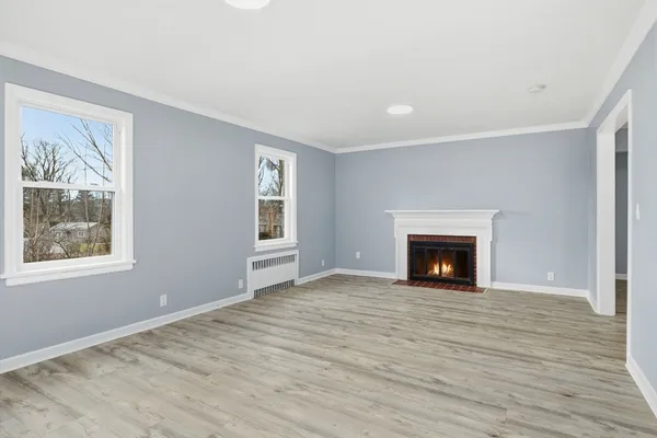 a view of an empty room with wooden floor fireplace and a window