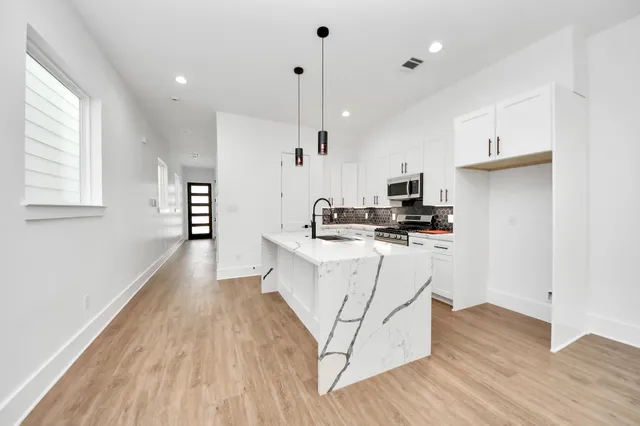 a kitchen with stainless steel appliances white cabinets a sink a stove a refrigerator and a window