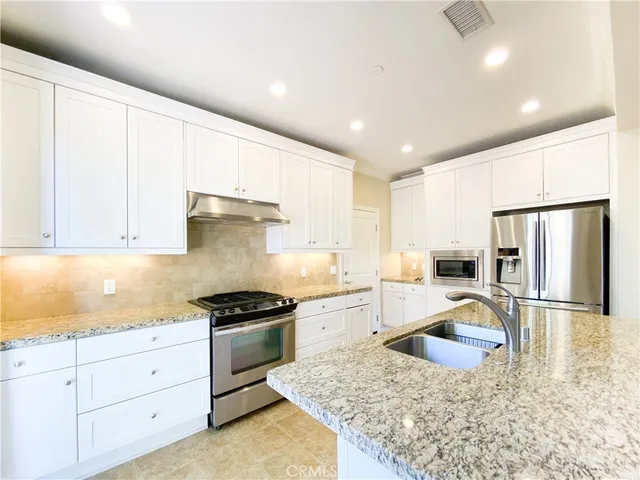 a kitchen with granite countertop a sink stainless steel appliances and white cabinets