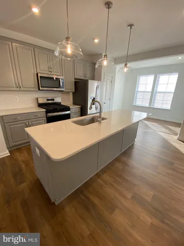 a large kitchen with stainless steel appliances a large counter top a stove a sink dishwasher a refrigerator and a dining table with wooden floor
