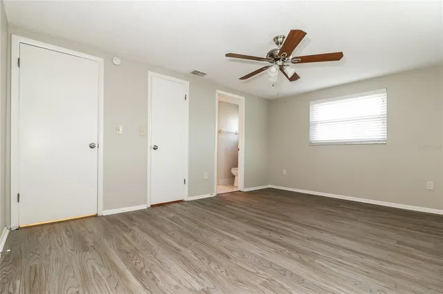 an empty room with wooden floor a ceiling fan and windows