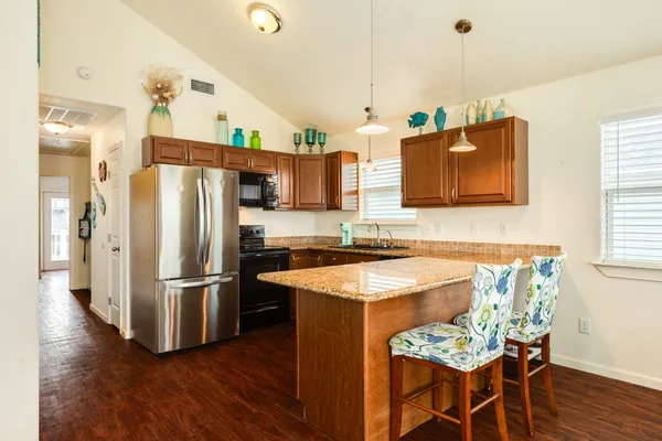 a kitchen with stainless steel appliances granite countertop a refrigerator a sink dishwasher a stove and a dining table with wooden floor