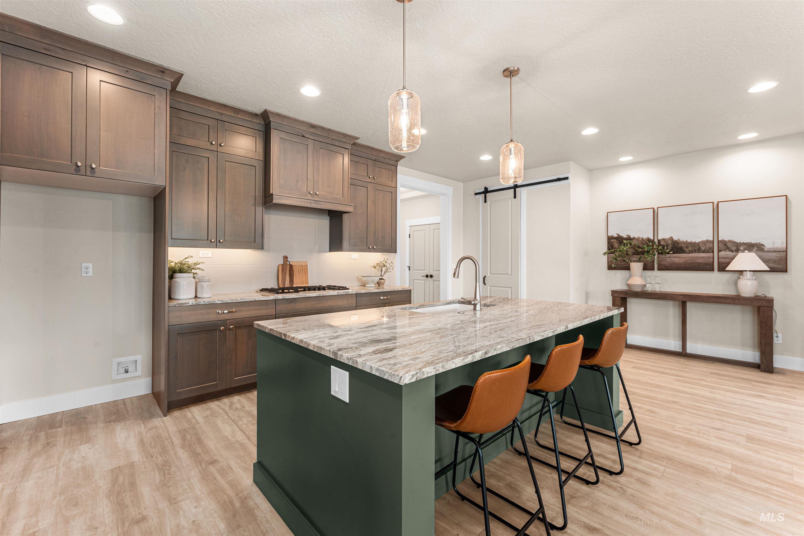 8082 Tandy Cv Street Middleton, ID 83644 - Photo 11 of 37 Kitchen featuring light stone countertops, light wood finished floors, pendant lighting, a barn door, and a kitchen breakfast bar