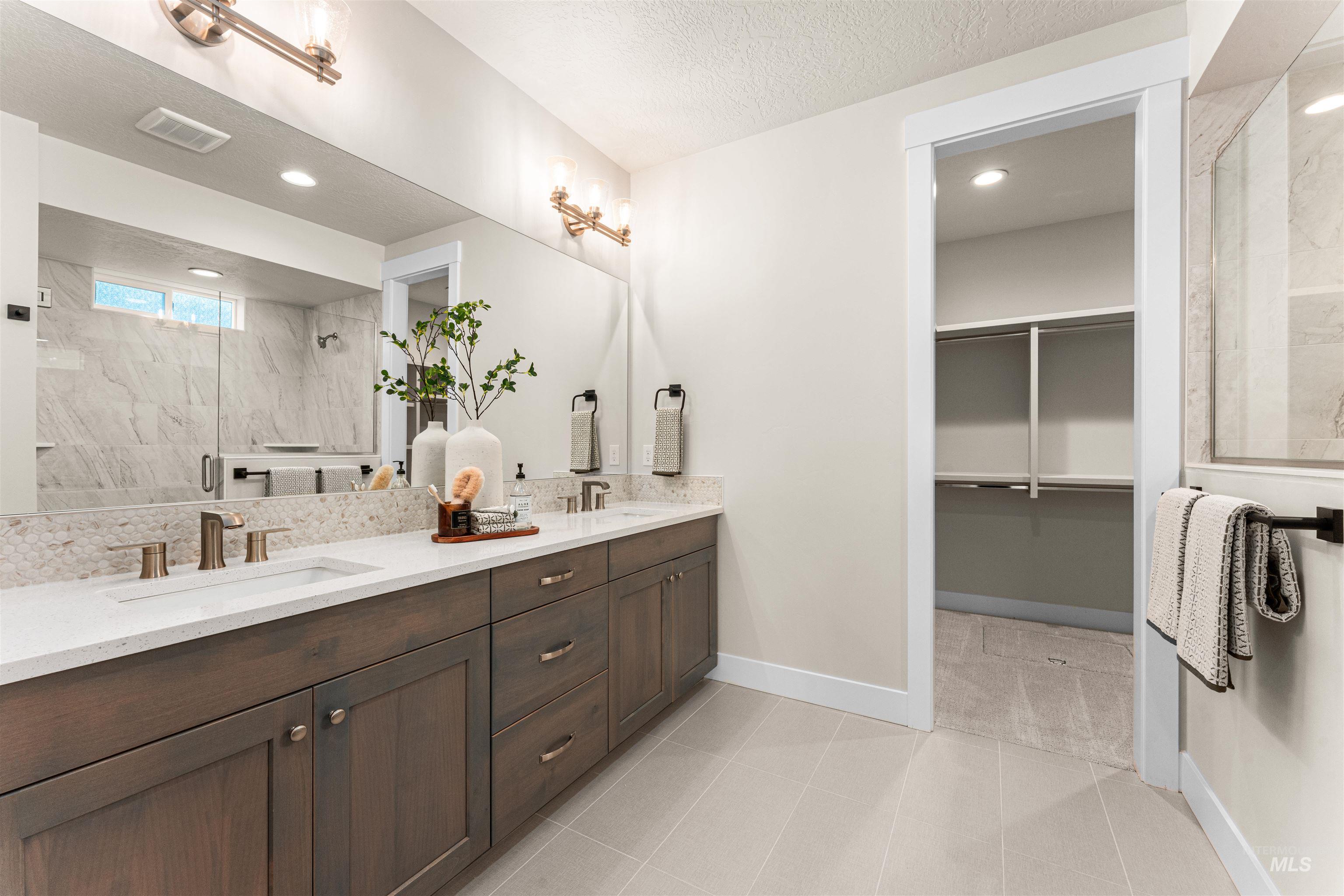 8082 Tandy Cv Street Middleton, ID 83644 - Photo 18 of 37 Bathroom with double vanity, a shower stall, a walk in closet, light tile patterned floors, and a textured ceiling
