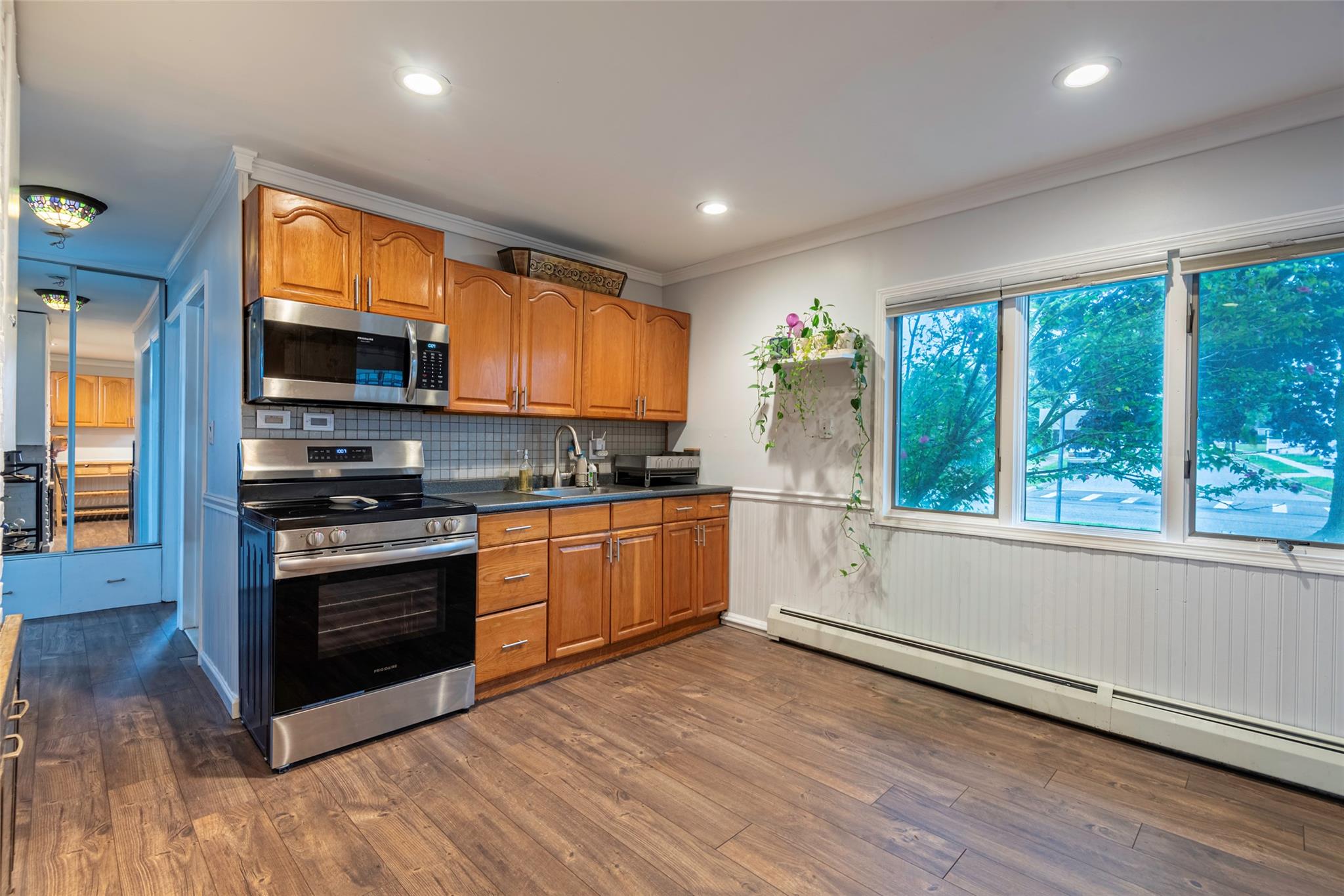22 Lowland Road Levittown, NY 11756 - Photo 5 of 38 Kitchen featuring appliances with stainless steel finishes, decorative backsplash, dark wood finished floors, wainscoting, and brown cabinetry
