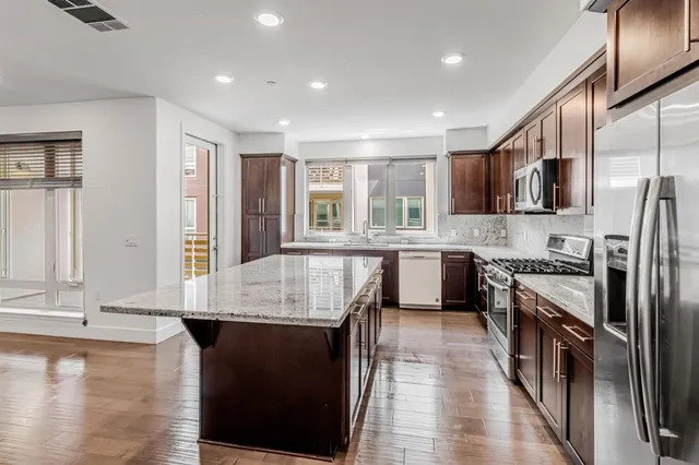 a large kitchen with stainless steel appliances granite countertop a stove a sink dishwasher a microwave oven and a refrigerator with wooden floor