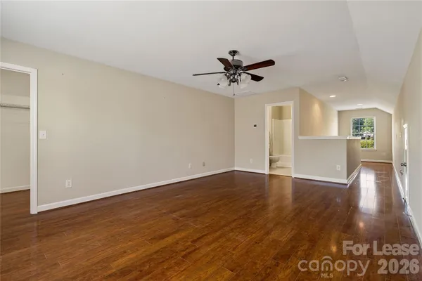 a view of an empty room with wooden floor and a ceiling fan