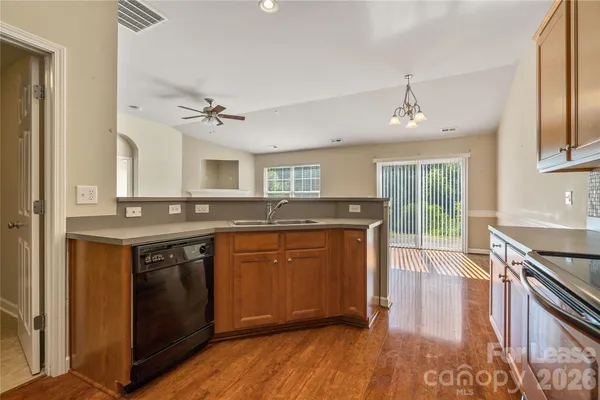 a kitchen with stainless steel appliances granite countertop wooden cabinets a stove a sink and dishwasher with wooden floor