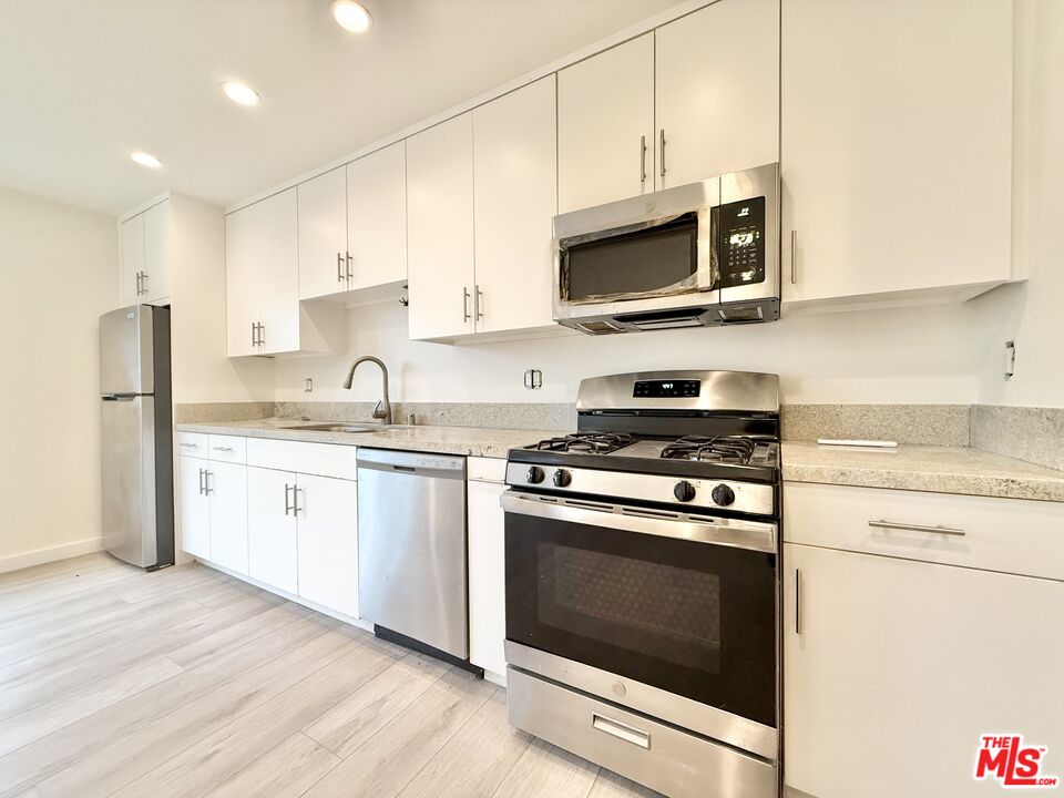 a kitchen with stainless steel appliances white cabinets a stove top oven a sink and dishwasher