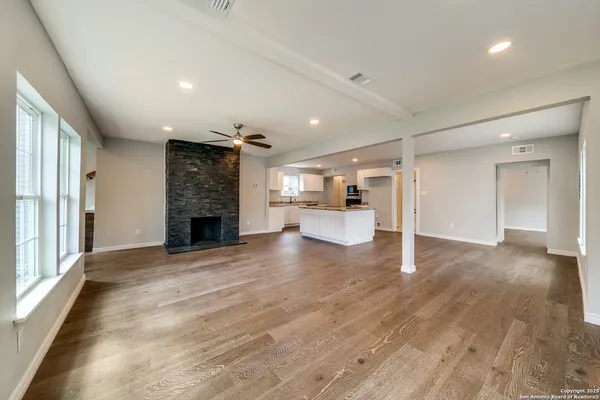 an empty room with wooden floor a ceiling fan and windows