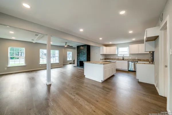 a large kitchen with stainless steel appliances granite countertop a large counter top a stove a sink a refrigerator white cabinets and wooden floor