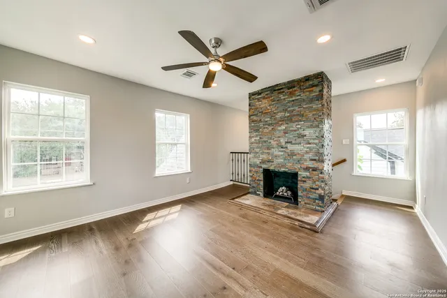 a view of an empty room with wooden floor a ceiling fan and windows