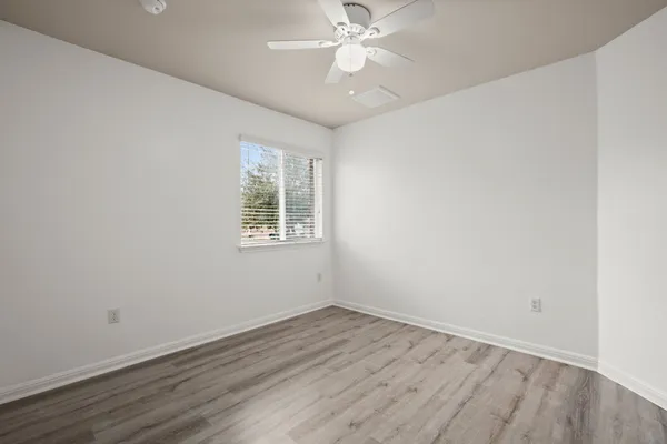 an empty room with wooden floor fan and windows